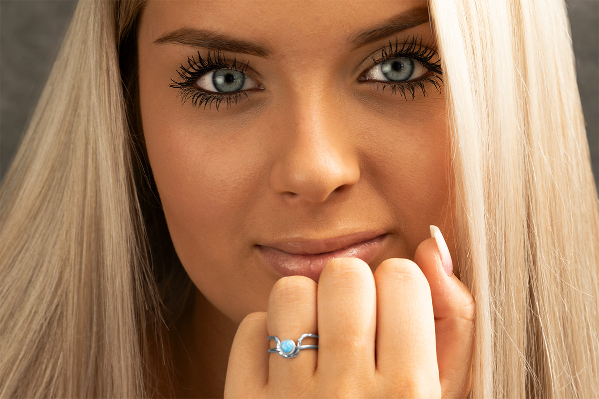 Close-up of a woman with blonde hair and blue eyes, wearing a Mind's Eye ring with blue opal by Rouaida.